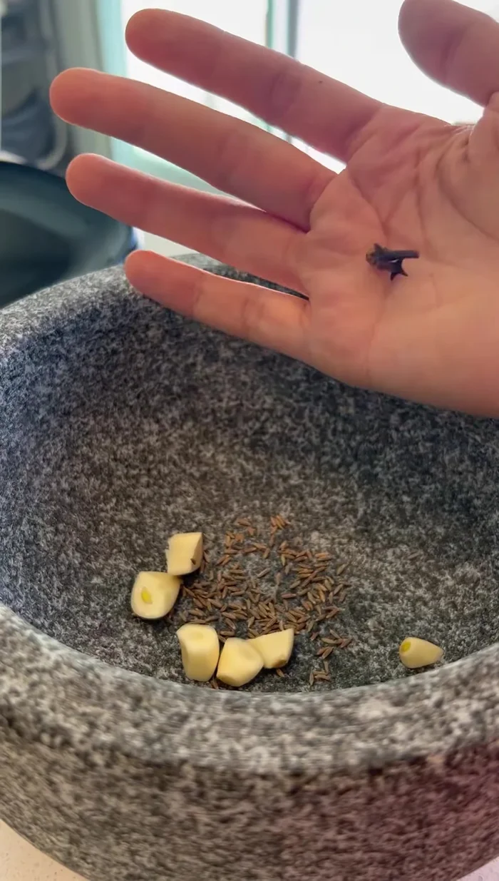 Prepare the spice mixture: crush two garlic cloves, cumin, cloves, and peppercorns with a little water.