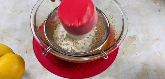 Add flour, baking powder, baking soda, cardamom powder (optional), vanilla or mango essence (optional), and salt. Sift the dry ingredients together.