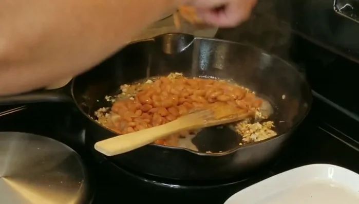 Add the refried beans and a piece of ham hock to the skillet; mash the ham hock into the beans.
