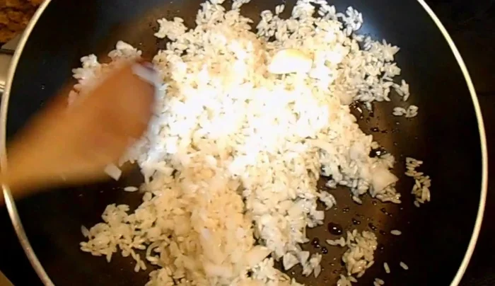 Add the chopped onion and garlic to the skillet and continue frying the rice until it's slightly darker.