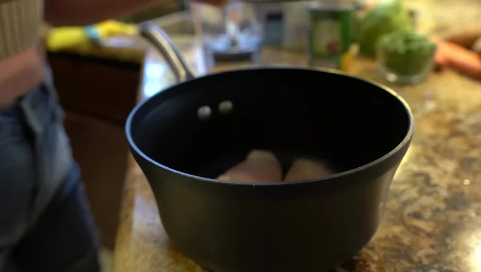 Add chicken to a pot with half a white onion, 2 garlic cloves, and salt. Cover with water.