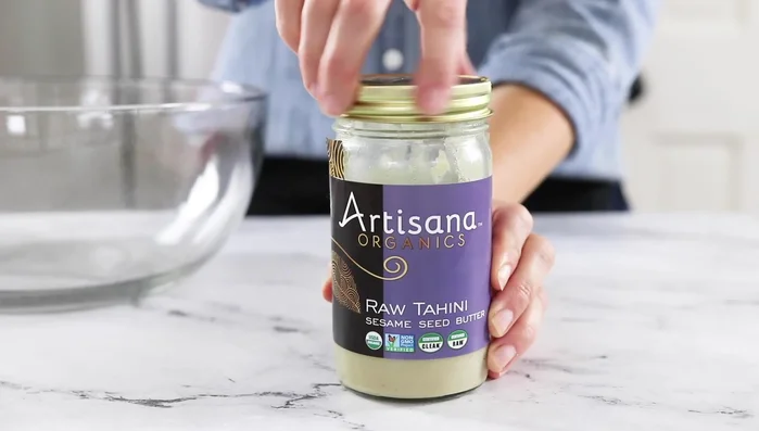 While cauliflower roasts, prepare the coleslaw. Combine tahini (or almond butter), lime juice, minced garlic (or garlic powder), salt, maple syrup, and water in a bowl. Whisk until smooth and creamy. Add more water if needed.