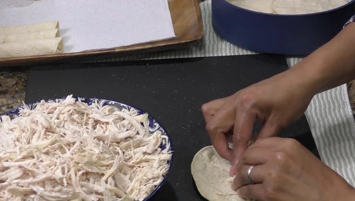 Assemble tacos with shredded chicken, lettuce, onion, tomato, cheese, and avocado sauce.