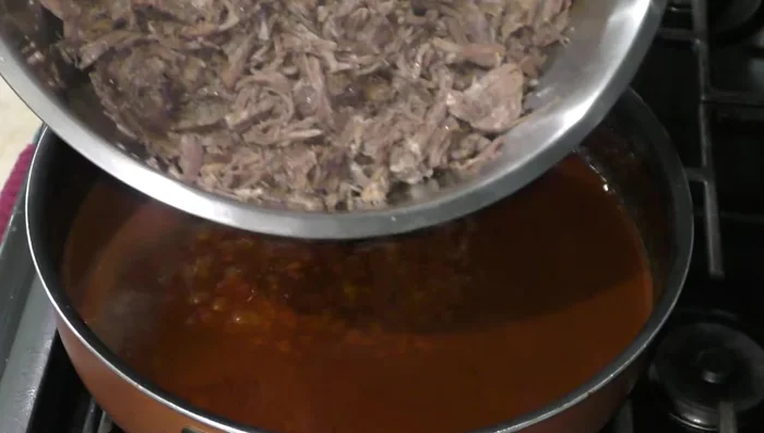 Shred the cooked pork and add it to the sauce. Reserve some of the sauce for later.