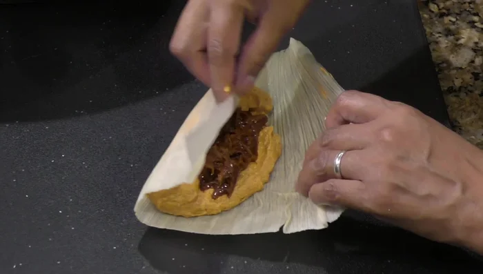 Prepare the tamales: Spread masa on corn husks, add meat filling, fold, and steam for 1 hour and 45 minutes.