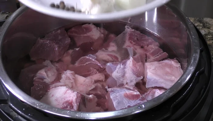 Cook 4kg pork shoulder in a pressure cooker with thyme, marjoram, allspice, half an onion, and a head of garlic for about 35 minutes.