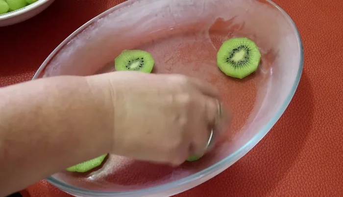 Blanch the kiwis in boiling water with sugar for 2 minutes to help the gelatin set better. Arrange the kiwis, strawberries, and some of the other fruits in the chilled refractory dish.