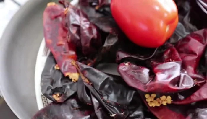 In a pan, fry 20 guajillo chilies and 3 tomatoes with a piece of onion. Remove the stems from the chilies (optional: remove seeds).
