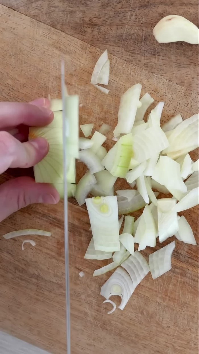 Finely chop an onion and set aside. Slice three cloves of garlic, half a yellow pepper, half a red pepper, and half a green pepper. Place everything on a plate.
