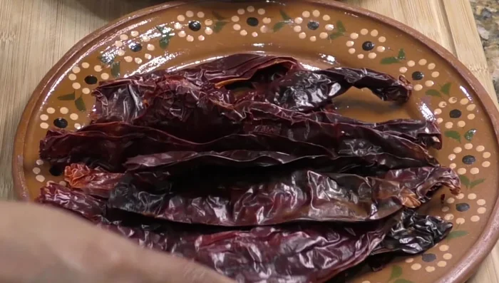 Prepare the sauce: Remove seeds from guajillo chiles. (67.159) Sauté the chiles, coriander, cloves, cumin, allspice, peppercorns, bay leaves, thyme, marjoram, garlic, and onion until golden brown. (179.48) Add water, cover, and simmer until soft. (211.68)