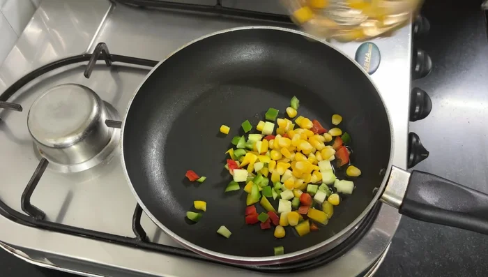 In a pan, heat 1 tablespoon of oil. Add bell peppers, zucchini, corn, salt, chili flakes, oregano, and red chili sauce.