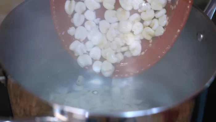 In a large pot, boil the corn in plenty of water (175.92). Add the onion and garlic, split in half (194.519). Season with salt once the corn begins to pop (201.72). Cover and cook.