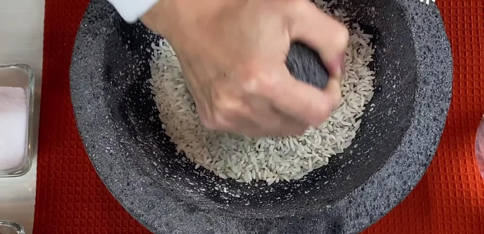 Add 1/3 cup of raw rice to the molcajete. Grind the rice into a powder. This will help polish the surface of the stone and remove excess dust.