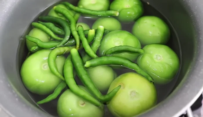 Boil 1 kilo of green tomatoes and green chilies (to your liking) in a saucepan until they change color.