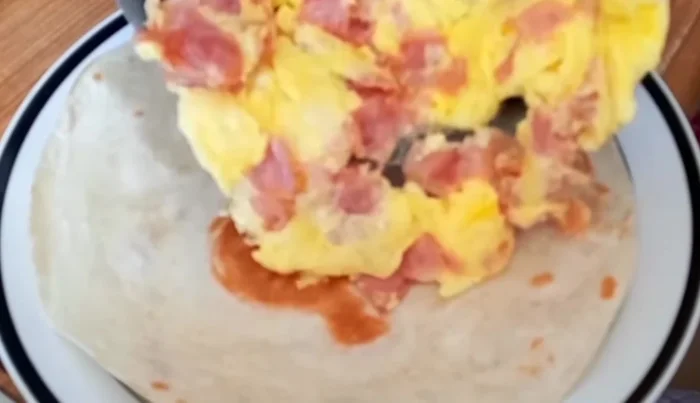 Place the cooked ham and egg on one end of the tortilla. Roll the tortilla, tucking in the ends (350.28).