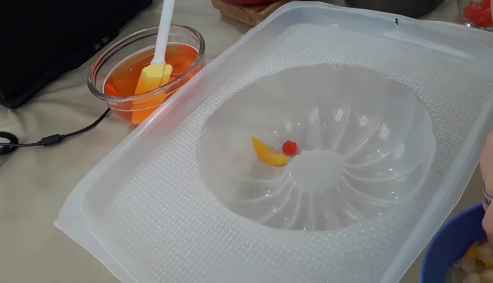 Remove the mold from the freezer. Layer the ingredients in the mold: start with some peach pieces in syrup, followed by a layer of transparent gelatin, then more fruits, and repeat.