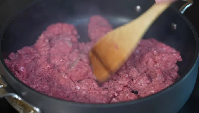 In a hot pan with little oil, fry the ground beef. Add chopped onion and garlic. Cook constantly, breaking down the meat evenly over medium-high heat.