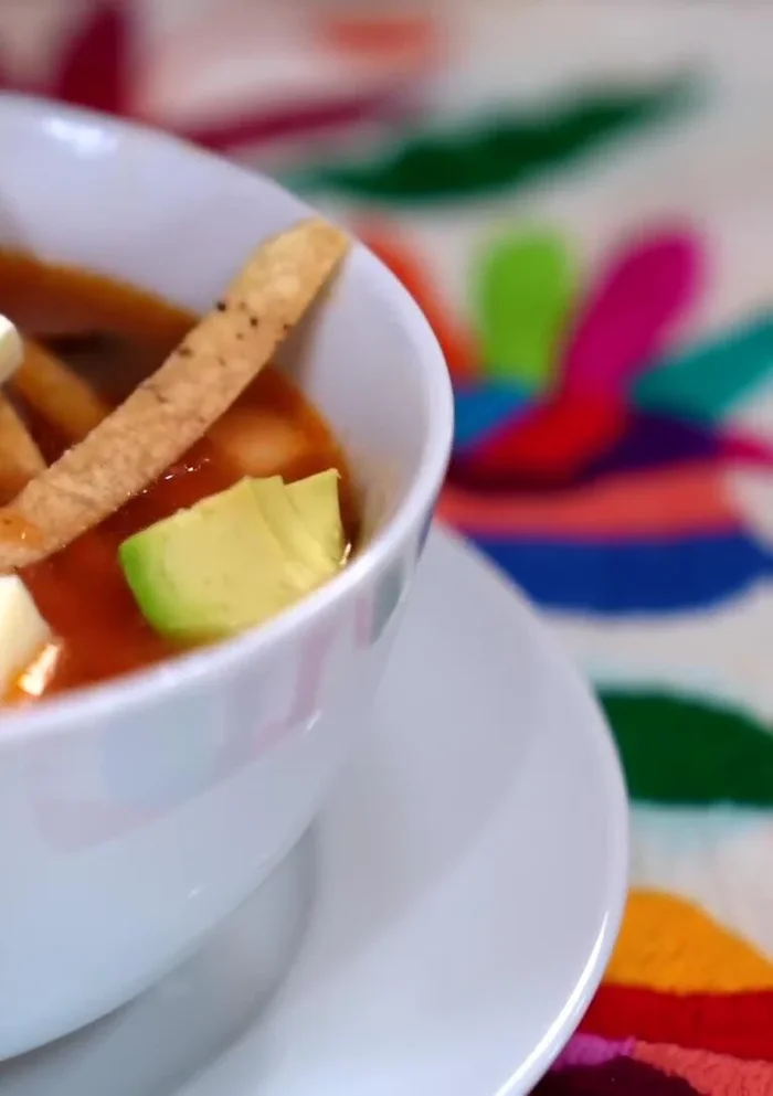 Serve the soup, garnished with fried tortilla strips, cheese, avocado, and cream.