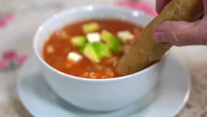 Serve the macaroni soup topped with cheese, avocado, the golden tacos, cream, and salsa macha.