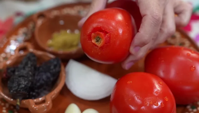 Prepare the sauce: Remove stems from tomatoes. In a molcajete, combine salt, a raw garlic clove, cumin, oregano, and crush.