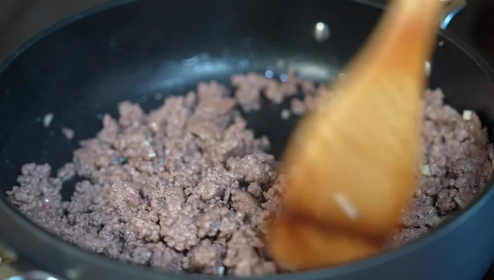 Once the meat is cooked, add the chopped onion and cabbage. Continue stirring.