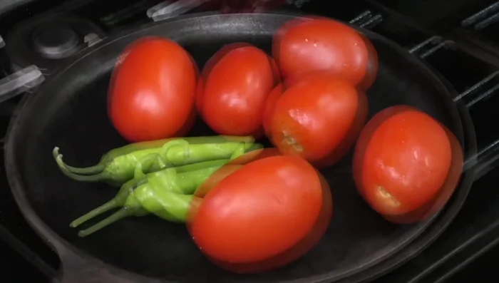 Roast tomatoes and serrano peppers on a griddle. Be careful not to burn the guajillo chili. (102.04)