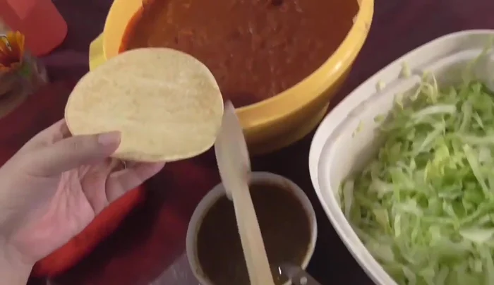 Assemble the tostadas: layer marinated beans, shredded pork, salsa, lettuce, onion, cream, and cheese.