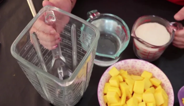 In a blender, combine half a cup of sugar, one cup of water, and the chopped mangoes.