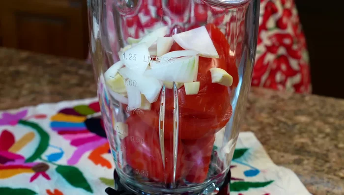 In a blender, combine the raw tomatoes, a piece of onion, garlic cloves, oregano, and the hydrated ancho chili. Add a little water to help blend. Blend until smooth.