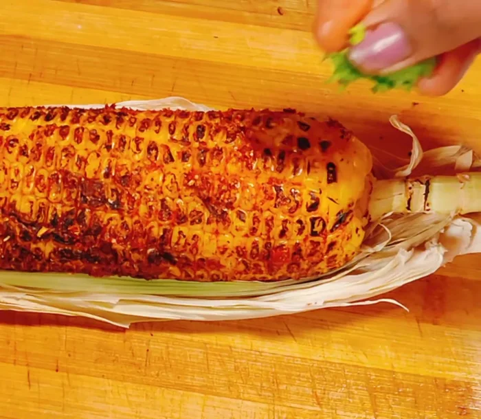 Prepare Tandoori Corn: Apply the spicy masala to the cooked corn, squeezing lemon juice over it and rubbing it in. Add coriander leaves and chili oil (optional).