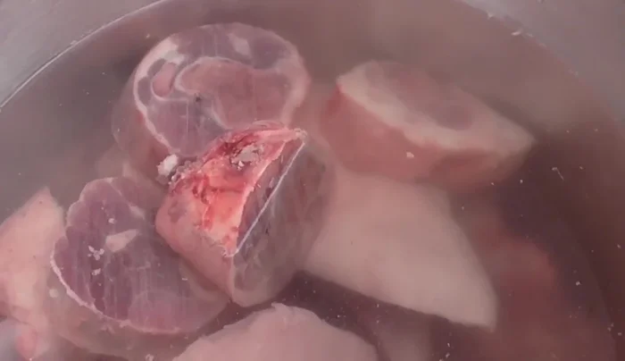 Clean the meat: Place the pig's head, pork leg, and bones in a bowl and consecutively change the water to remove excess blood. This ensures a whiter pozole.
