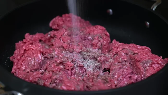 In a hot pan, brown the ground beef, adding the chopped garlic. Stir constantly to break up the meat.